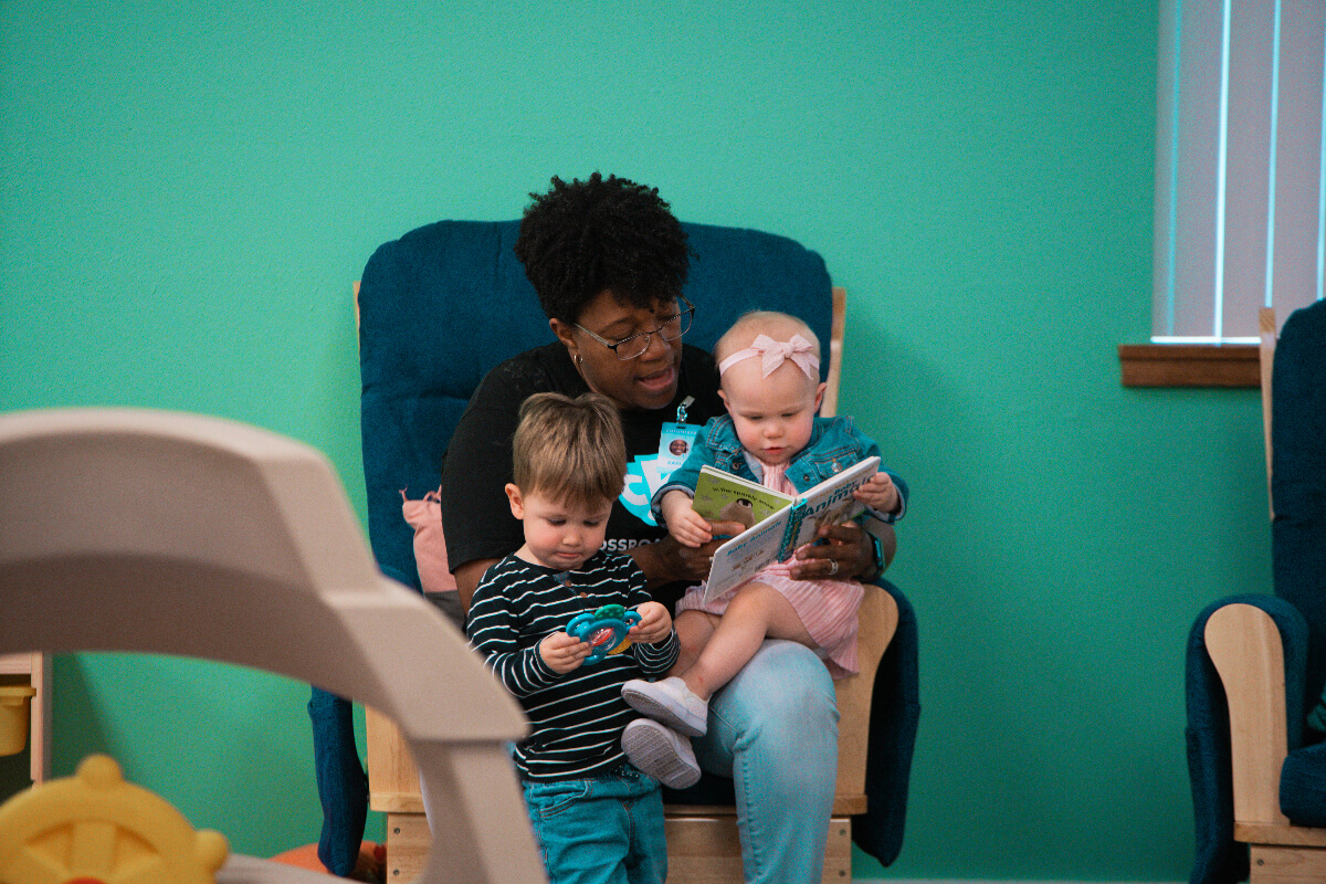 mom reading book to two kids on her lap